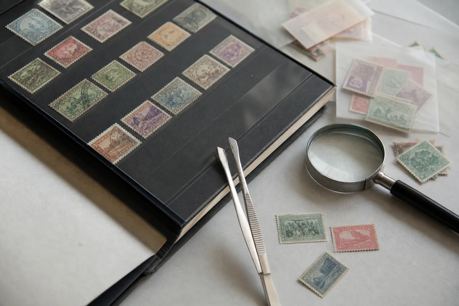 Matériel de philatélie avec album, pince et loupe pour examiner des timbres.